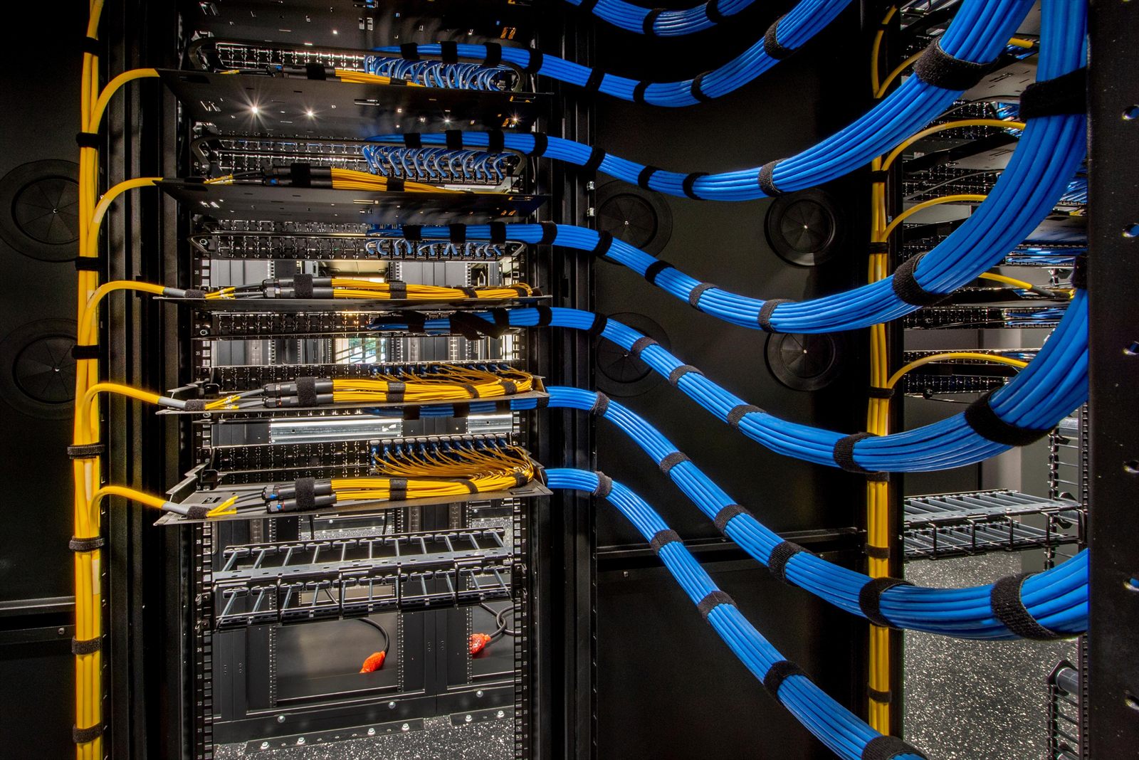 Network rack with blue and yellow patch cables dressed and velcro-bundled into patch panels