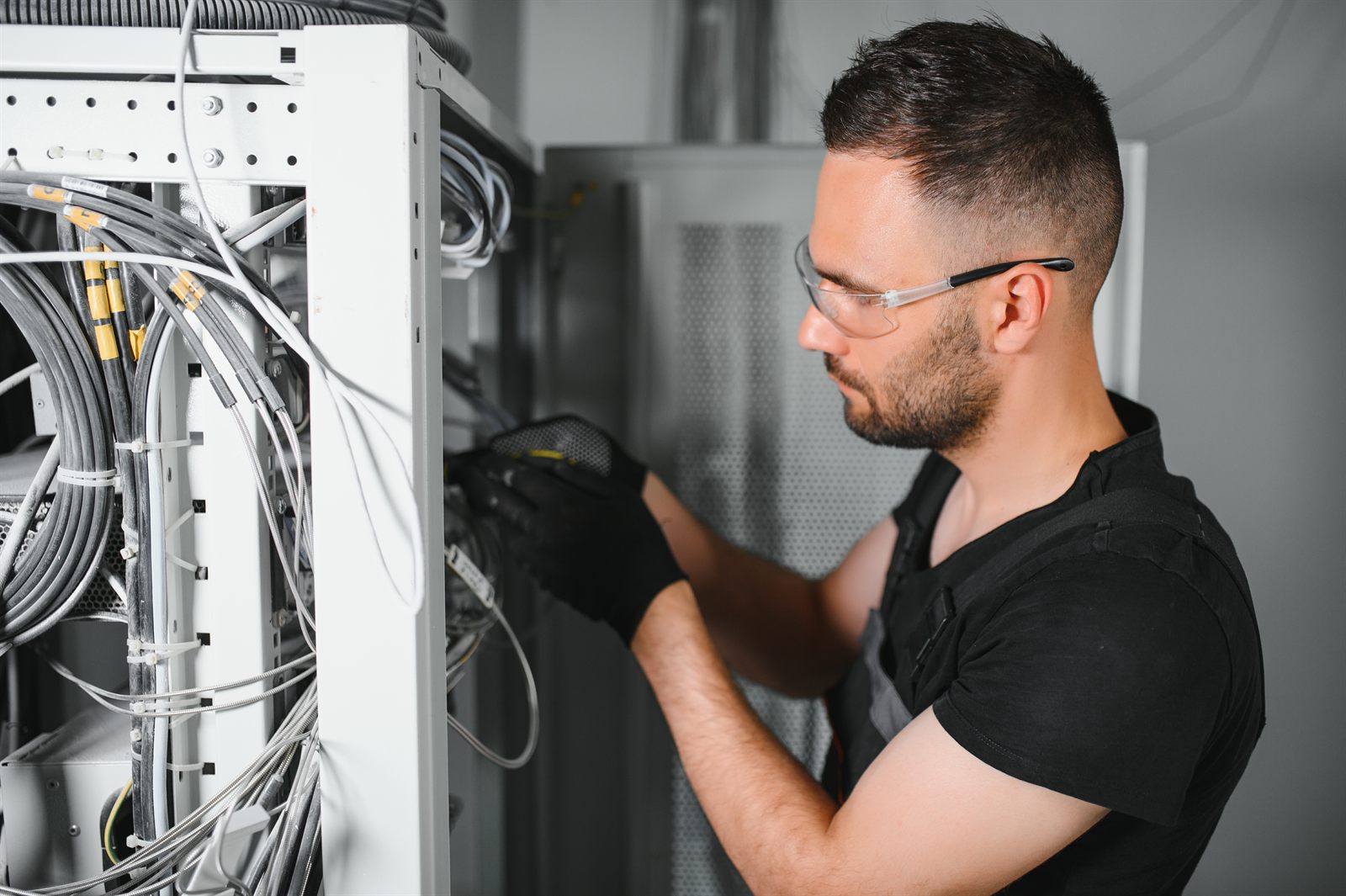 Technician in safety glasses terminating low-voltage cabling inside a wall-mounted enclosure