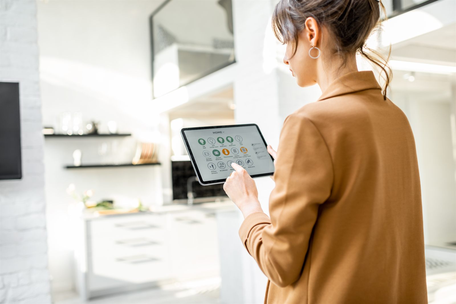 Person in a bright open-plan kitchen using a tablet to control lighting, heating and sockets room by room
