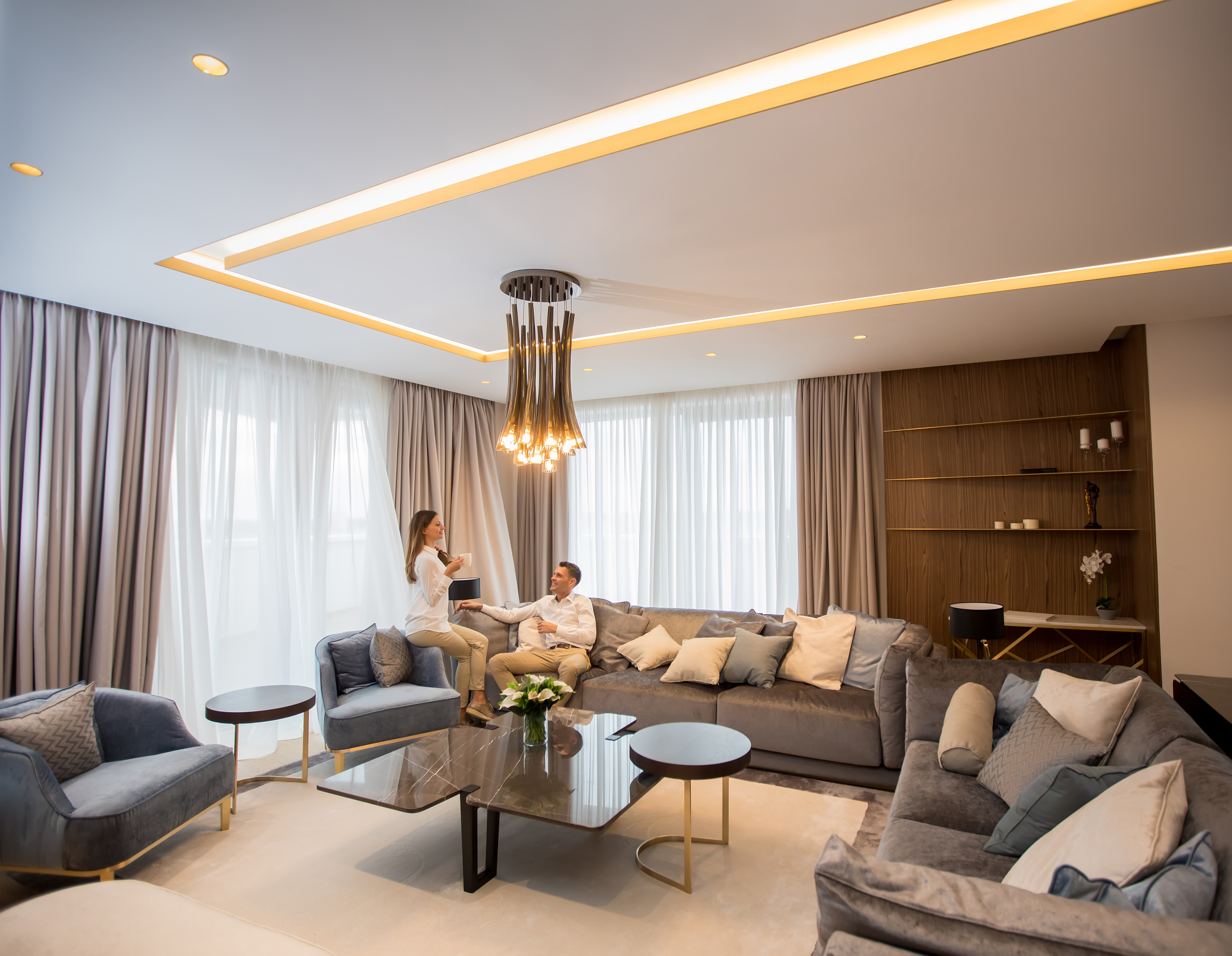 Open-plan living room with layered cove lighting and sheer motorized shades
